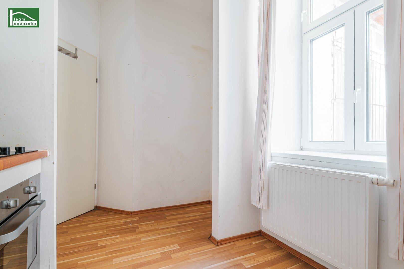 Blick von der Küchenzeile auf ein helles Fenster mit Heizkörper und Holzfußboden.