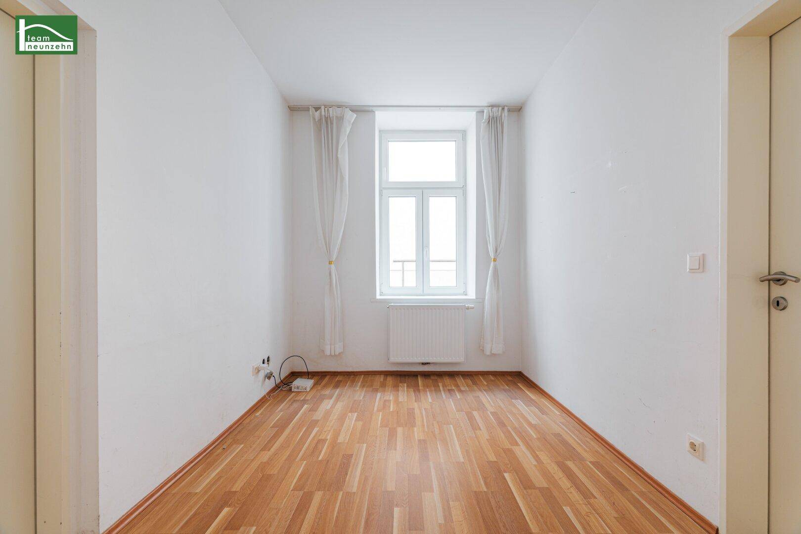 Helles, leeres Zimmer mit Holzfußboden und Fenster, bereit zur individuellen Gestaltung.