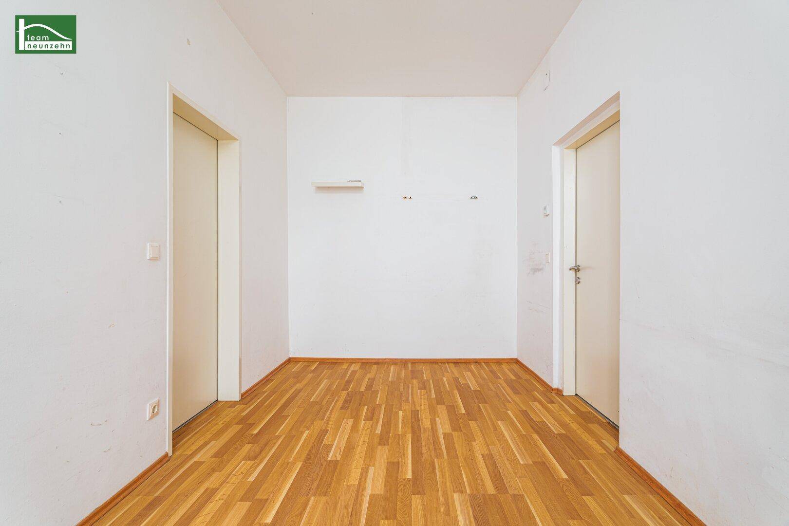 Leerer Flur mit hellem Holzfußboden und zwei Türen, der verschiedene Räume verbindet.
