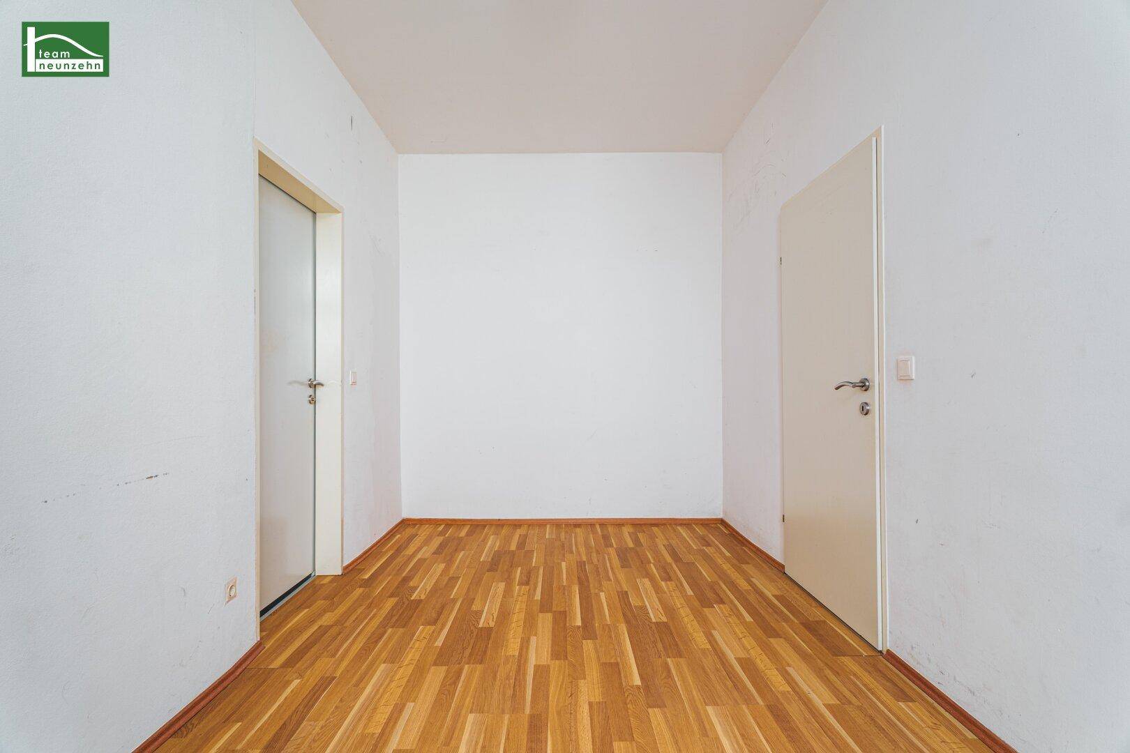 Leerer Flur mit hellem Holzfußboden und zwei Türen, der zu verschiedenen Räumen führt.