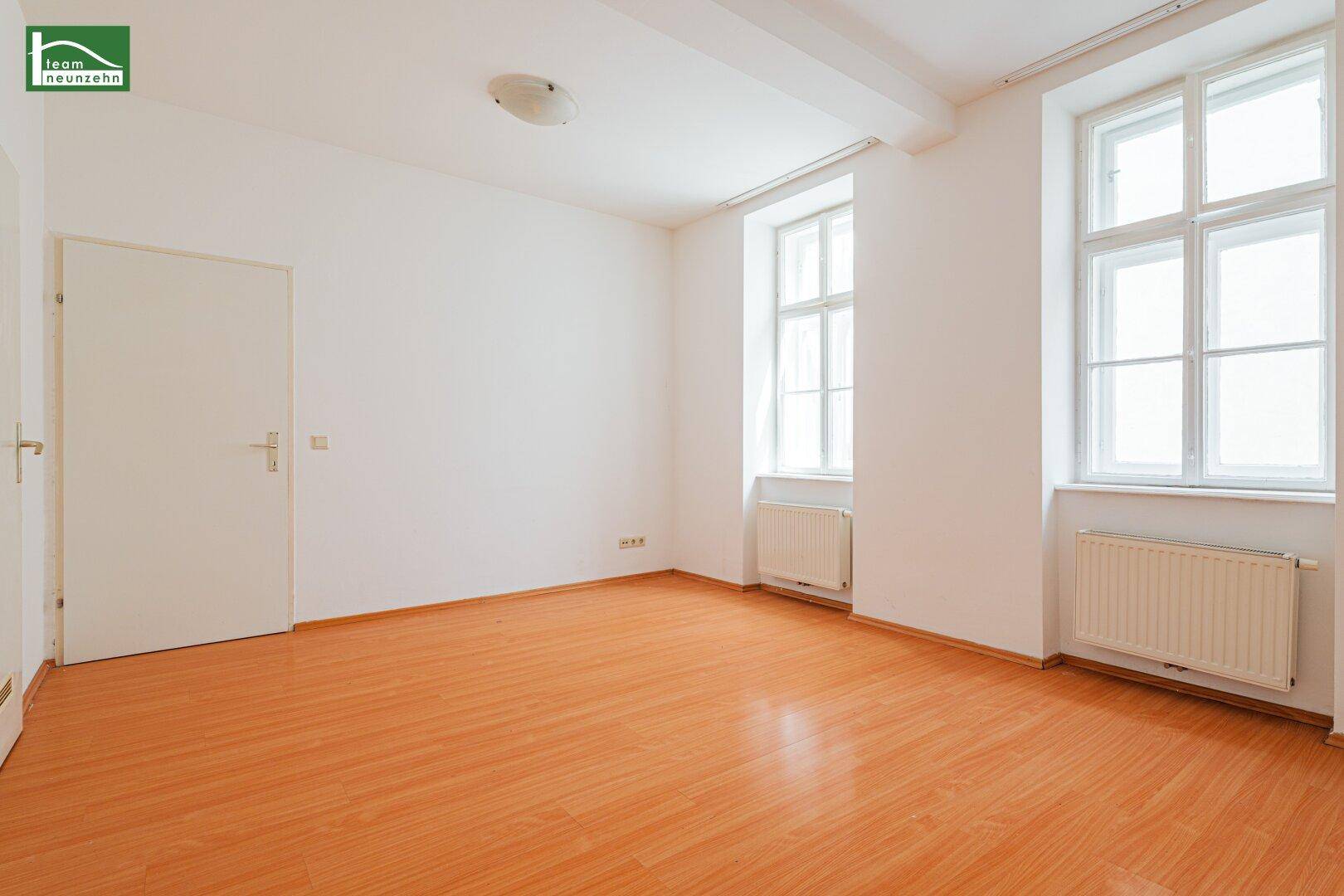 Helles Zimmer mit Holzboden, weißen Wänden und zwei großen Fenstern, ideal als Wohn- oder Schlafzimmer.