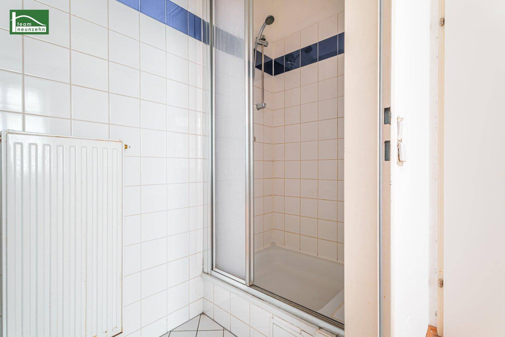 Badezimmer mit weiß gefliesten Wänden, Duschkabine und blauem Akzentstreifen.