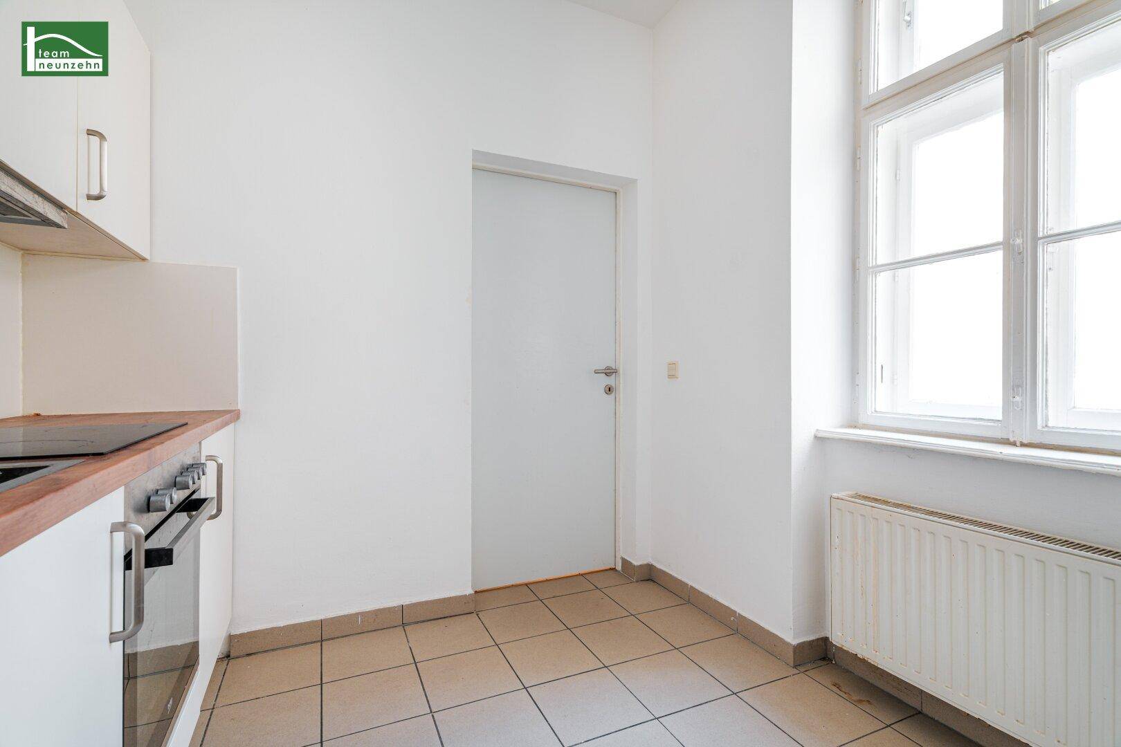 Helle Küchenzeile mit Fenster, weißen Schränken und gefliestem Boden, bietet ausreichend Arbeitsfläche.