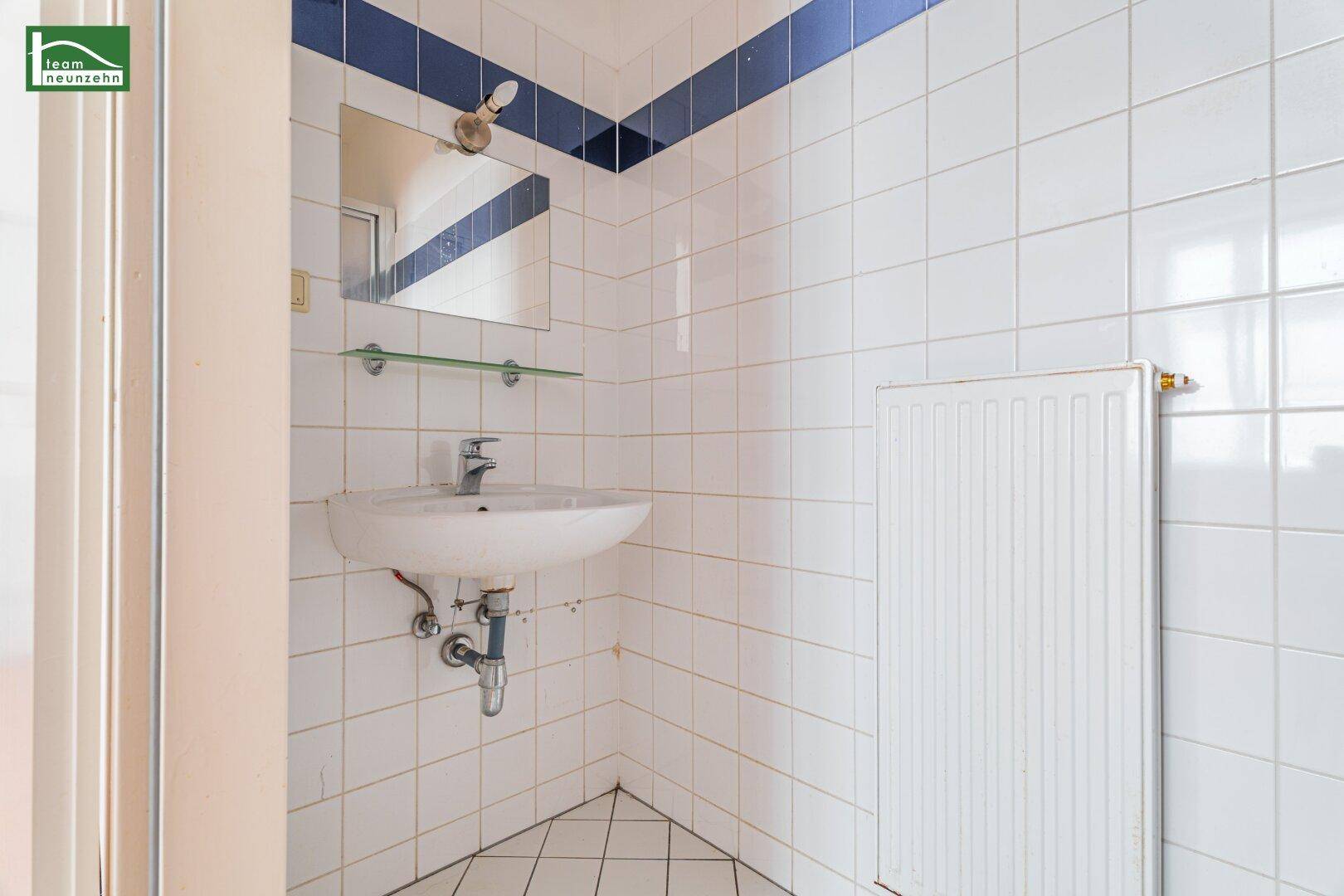 Waschbeckenbereich in einem gefliesten Badezimmer mit Spiegel und weiß-blauer Wandgestaltung.