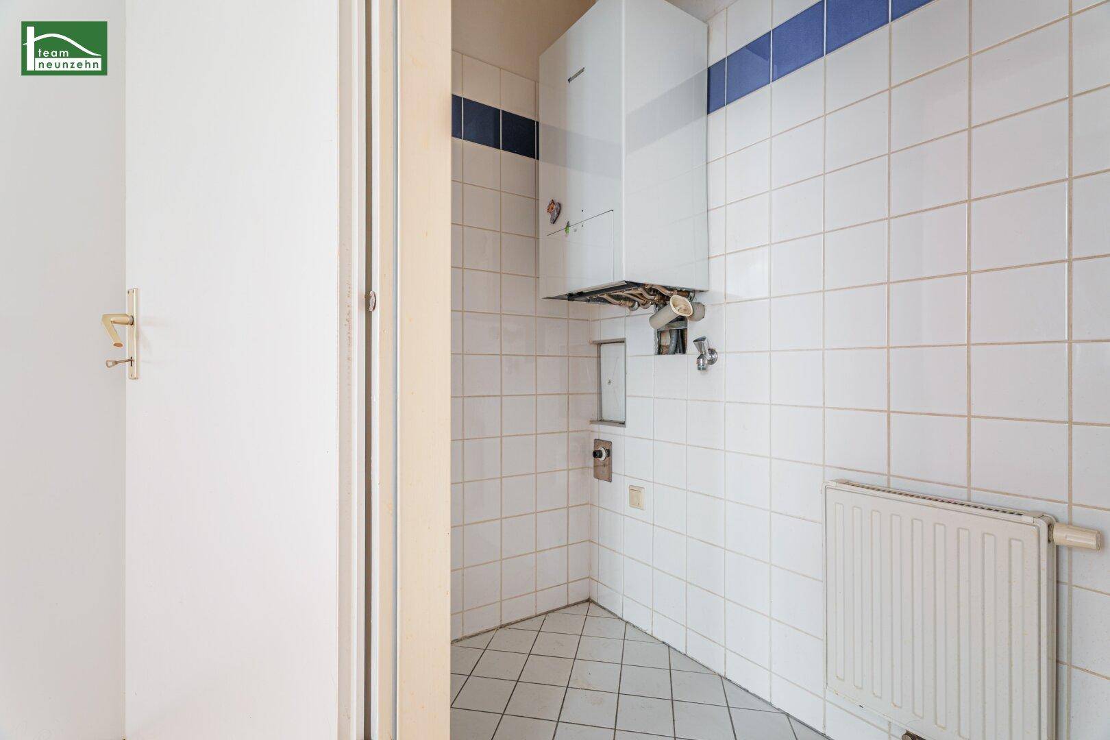 Warmwasserbereiter in einem gefliesten Raum mit weiß-blauen Akzenten und Heizkörper.
