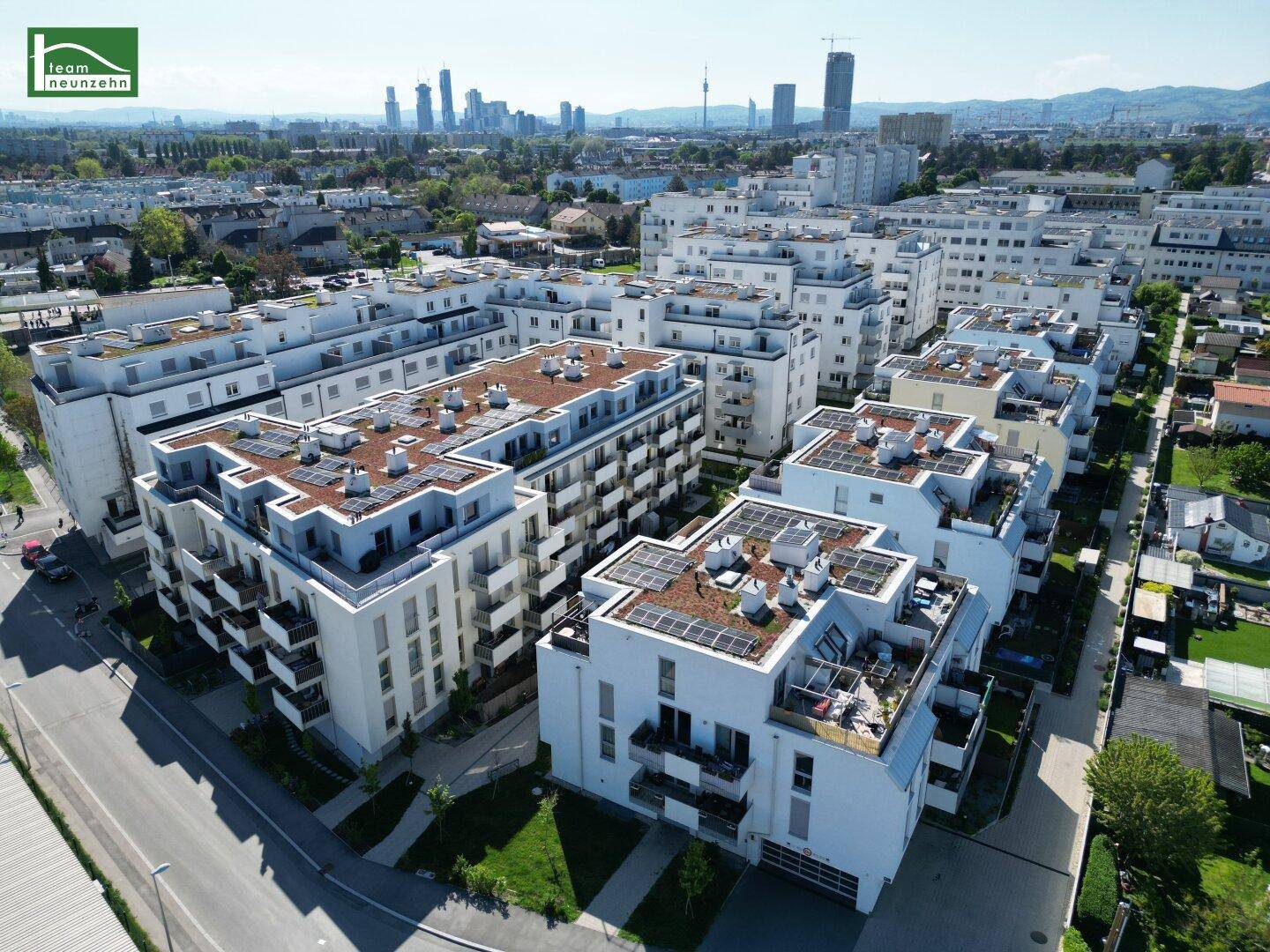 Luftaufnahme einer modernen Wohnanlage mit Flachdächern und Solarpaneelen in städtischer Umgebung.