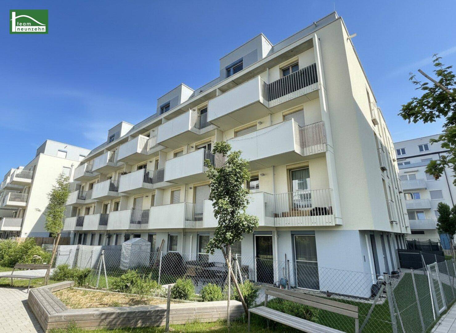 Außenansicht einer modernen Wohnanlage mit Balkonen und einem gemeinschaftlichen Gartenbereich.