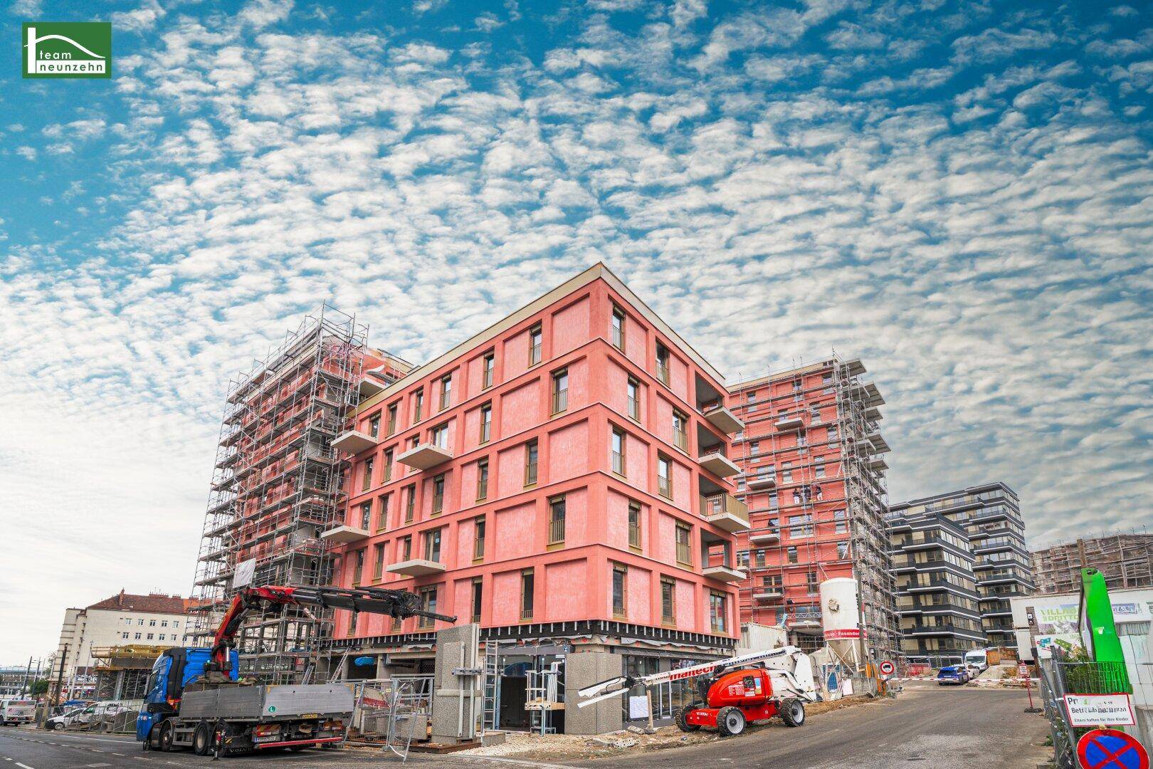 Neubaugebäude in Bauphase mit Gerüsten und Baukränen unter blauem Himmel, zeigt den Fortschritt.