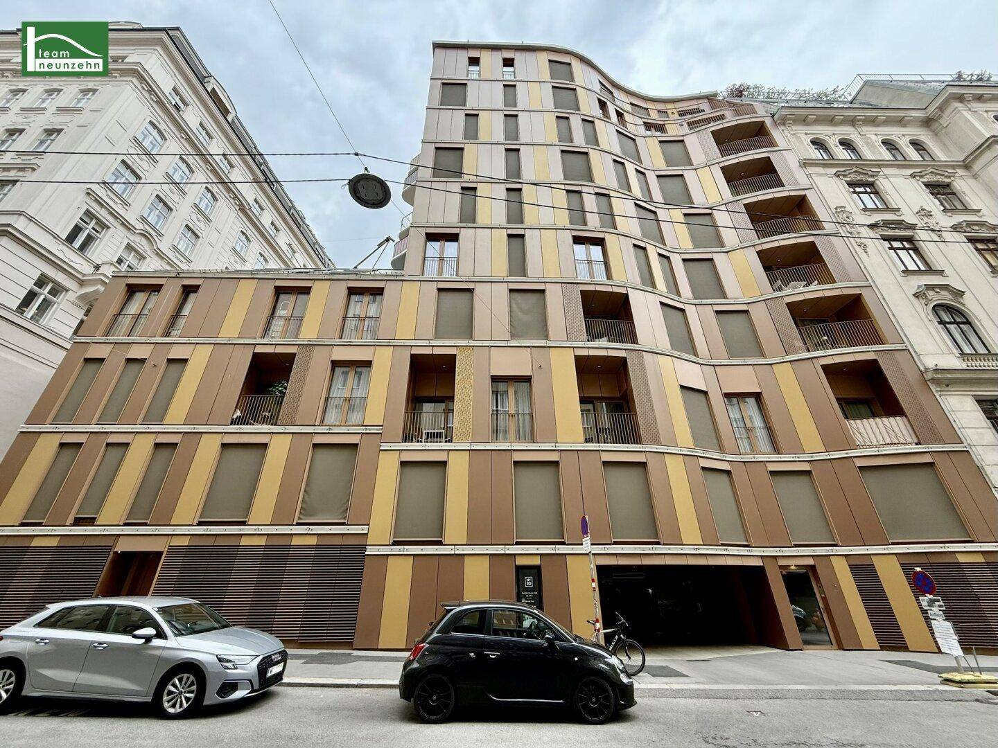 Moderne Gebäudefassade mit geschwungener Architektur, großen Fenstern und Außenjalousien an einer Stadtstraße.