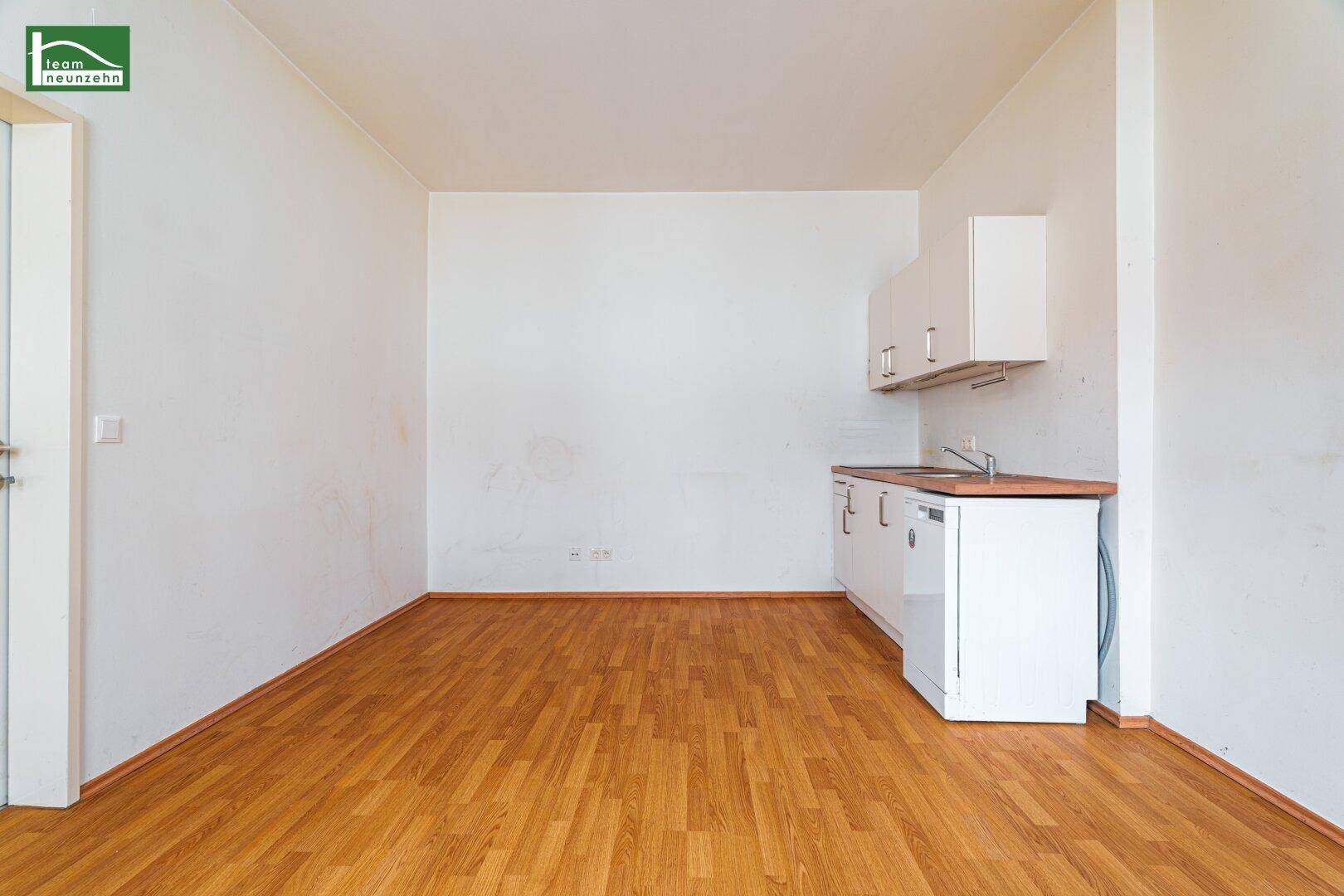 Einfache Küchenzeile in einem hellen Raum mit Holzboden und viel Platz.