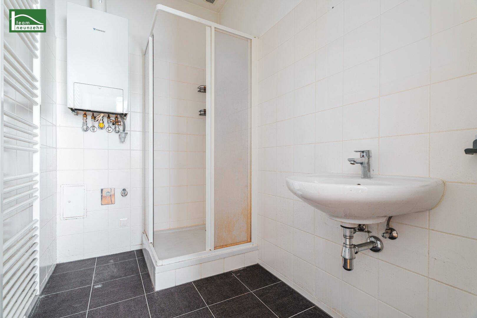 Badezimmer mit Duschkabine, Waschbecken, weißen Fliesen und dunklem Boden.