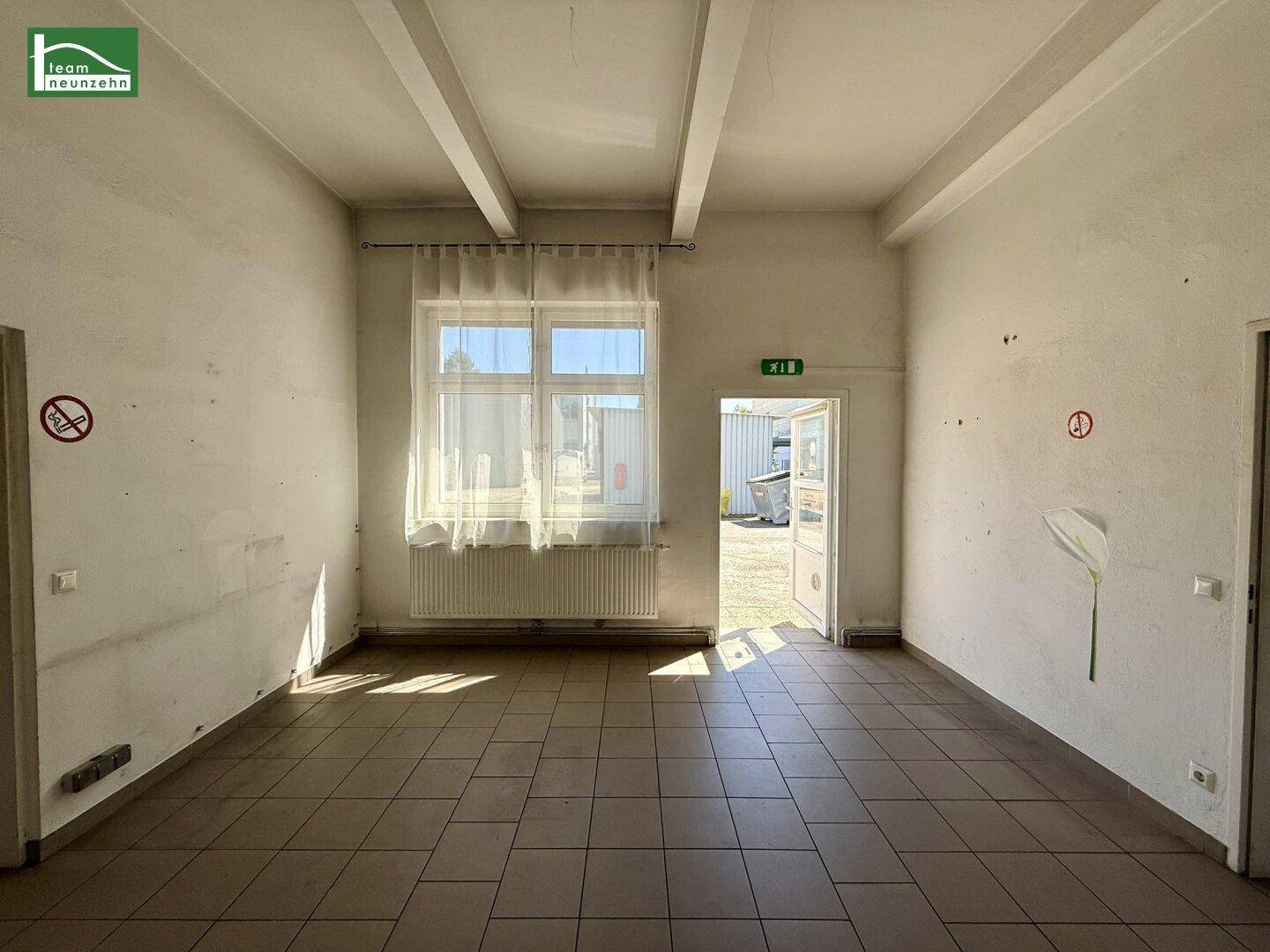 Helles Büro mit Fliesenboden, großem Fenster und Zugang zu einem Außenbereich.