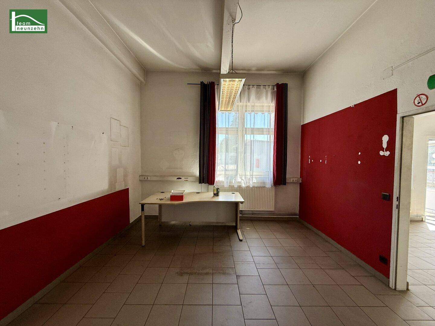 Büro mit roter Akzentwand, Fliesenboden und einem Schreibtisch unter einem großen Fenster.