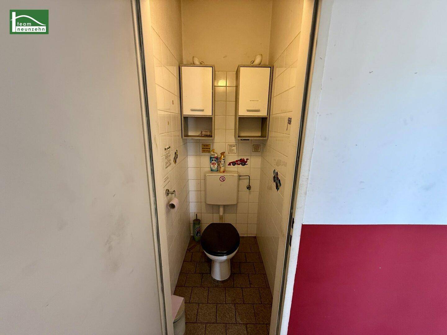 Kleine Gästetoilette mit Fliesenboden, Wandregalen und einem WC mit dunklem Sitz.
