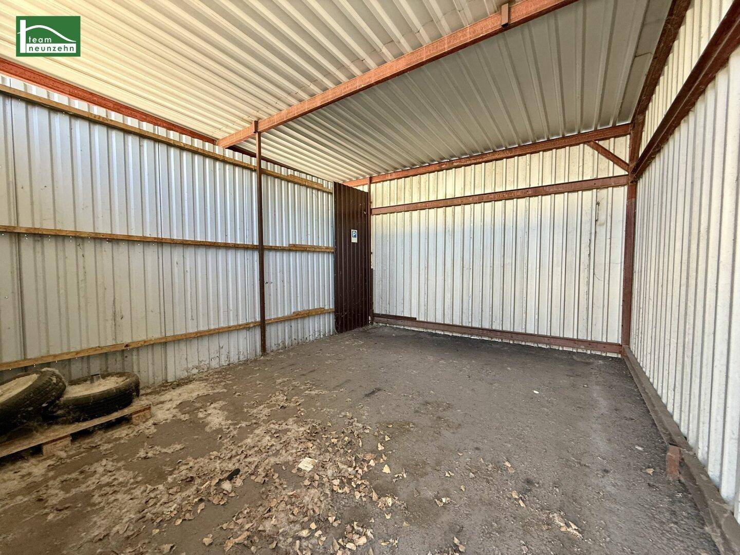 Offener Unterstand oder Carport mit Wellblechdach und Metallwänden, genutzt als Lagerfläche.