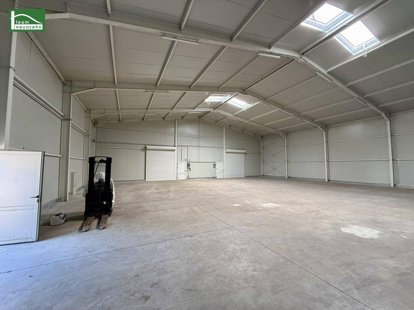 Große, leere Lagerhalle mit hohen Decken, Oberlichtern und einem Gabelstapler im Vordergrund.