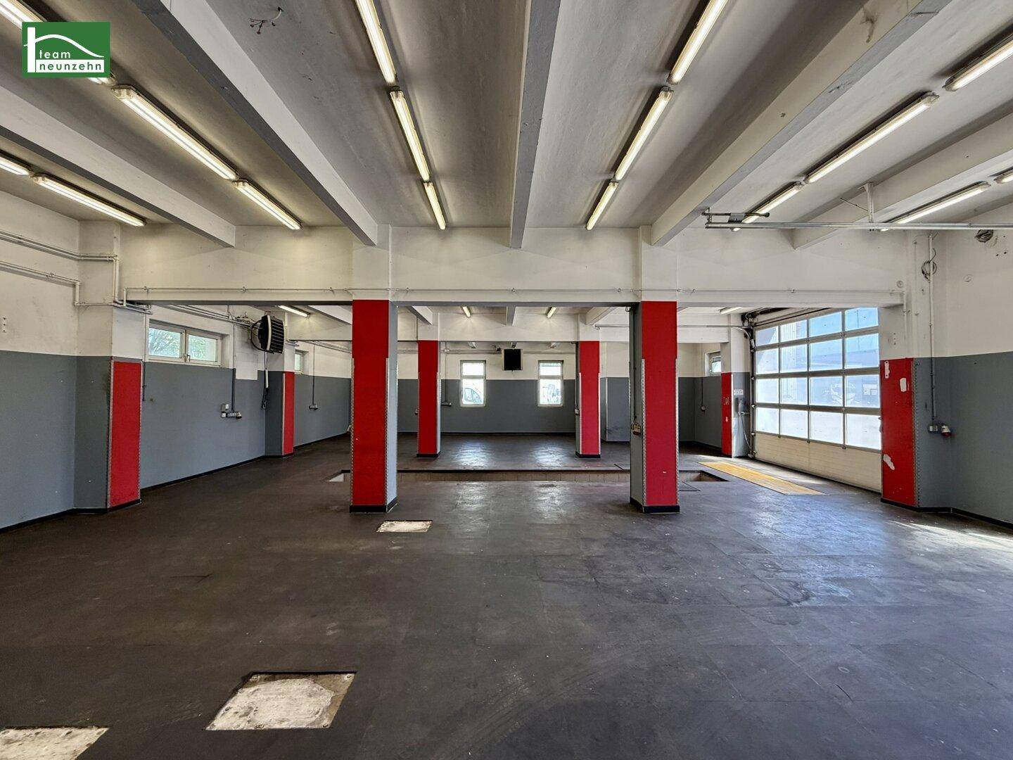 Große Werkstatthalle mit hohen Decken, roten Stützpfeilern und mehreren Garagentoren.