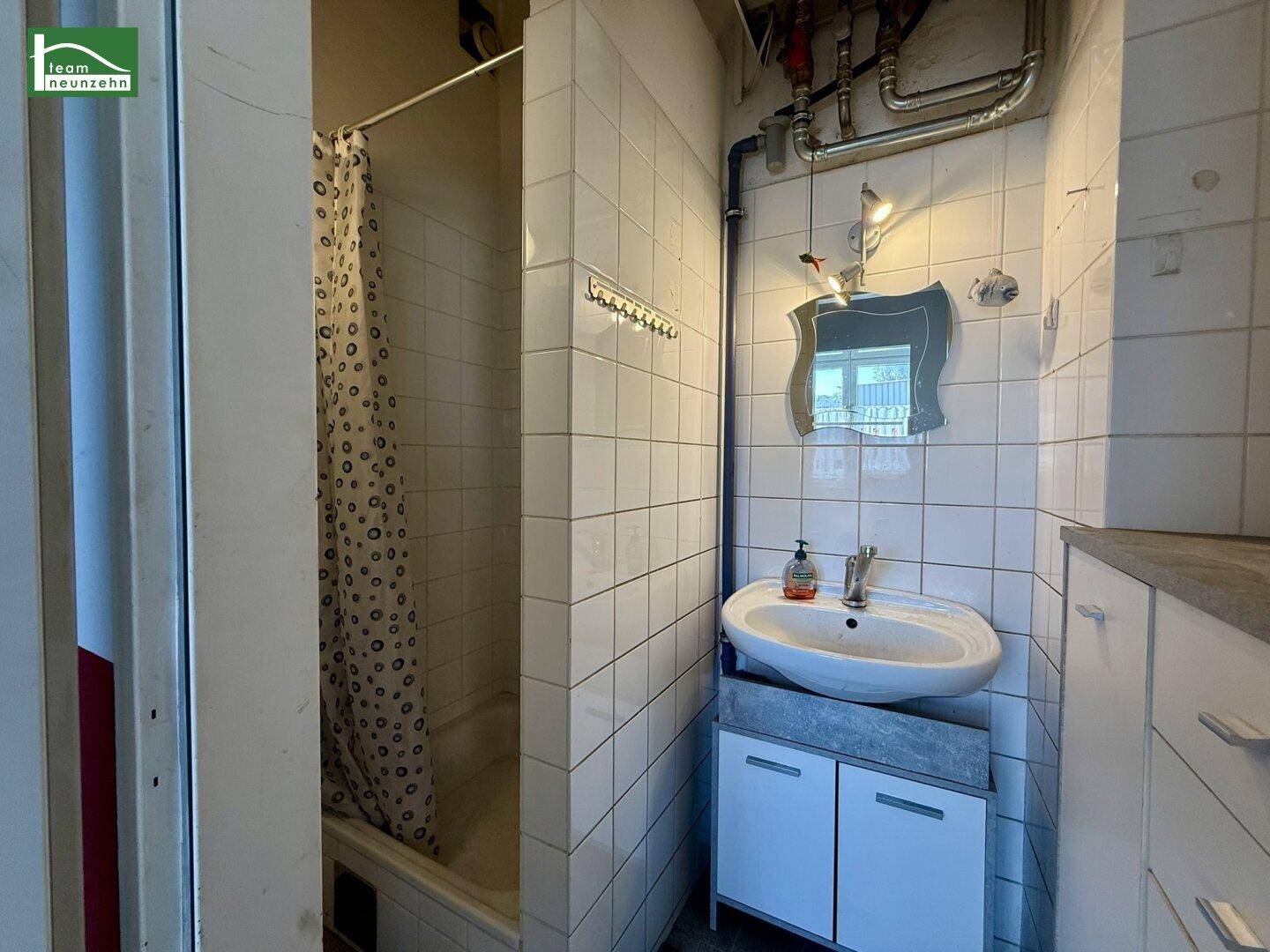 Badezimmer mit weißen Fliesen, Waschbecken, Spiegel und einer Badewanne mit Duschvorhang.