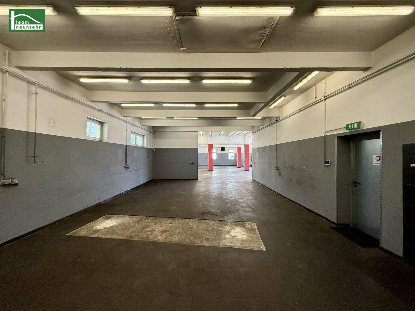 Geräumige Werkstatthalle mit hohen Decken, grauen Wänden und einem Eingangsbereich.