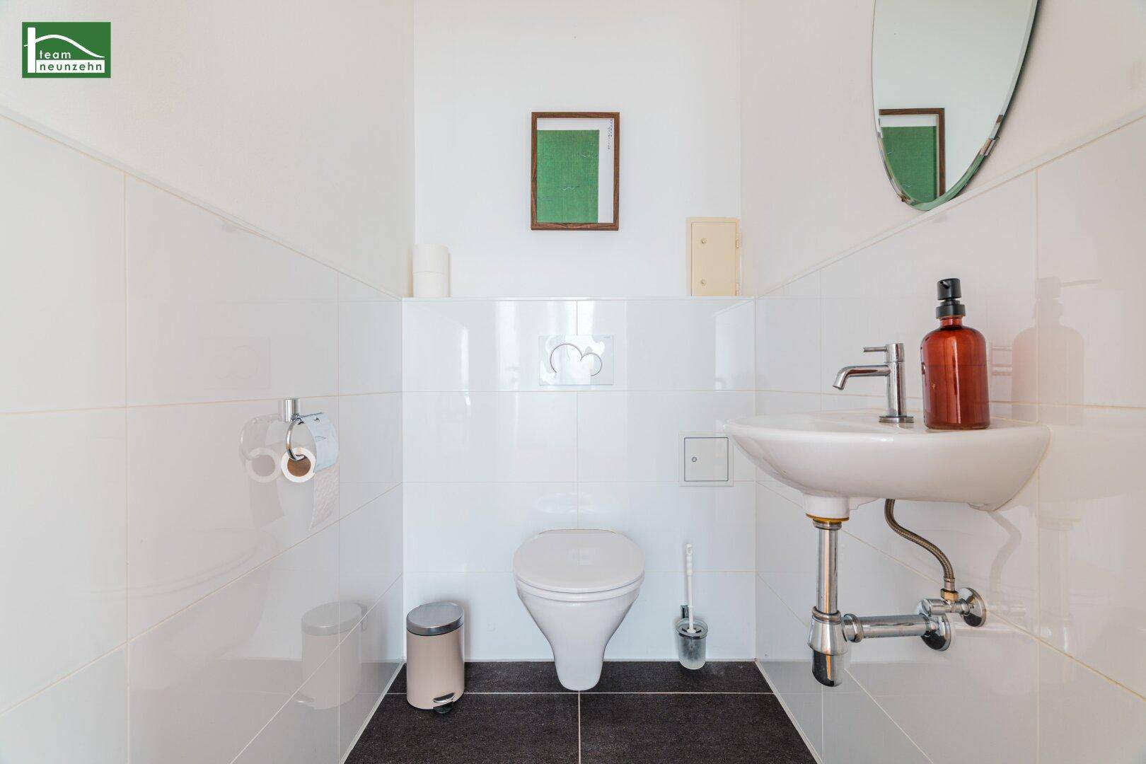 Modernes Gäste-WC mit weißen Fliesen, dunklem Boden und wandmontiertem WC.