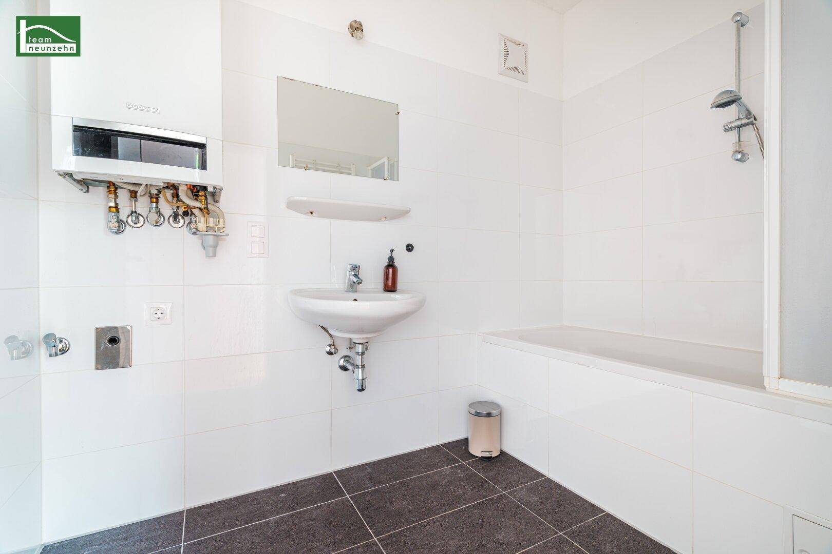 Helles Badezimmer mit Badewanne, Dusche und Waschbecken, ausgestattet mit weißen Fliesen.
