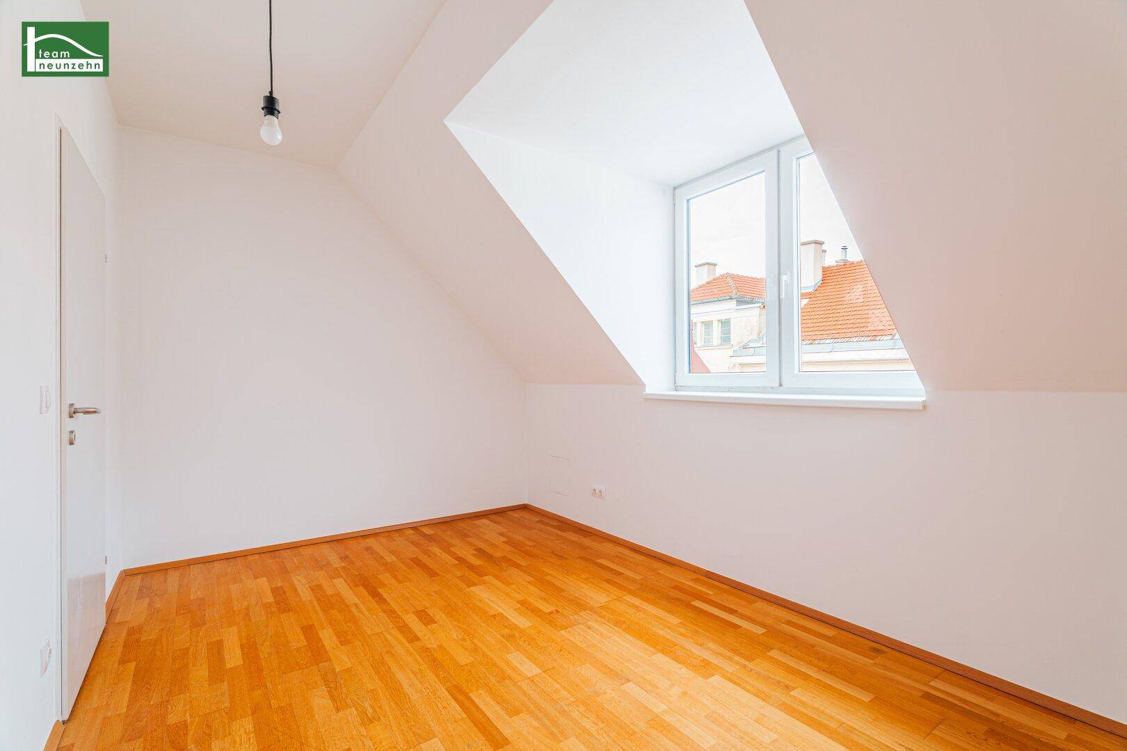 Helles Dachzimmer mit Holzboden und schrägen Wänden, bietet einen Blick über die Dächer.