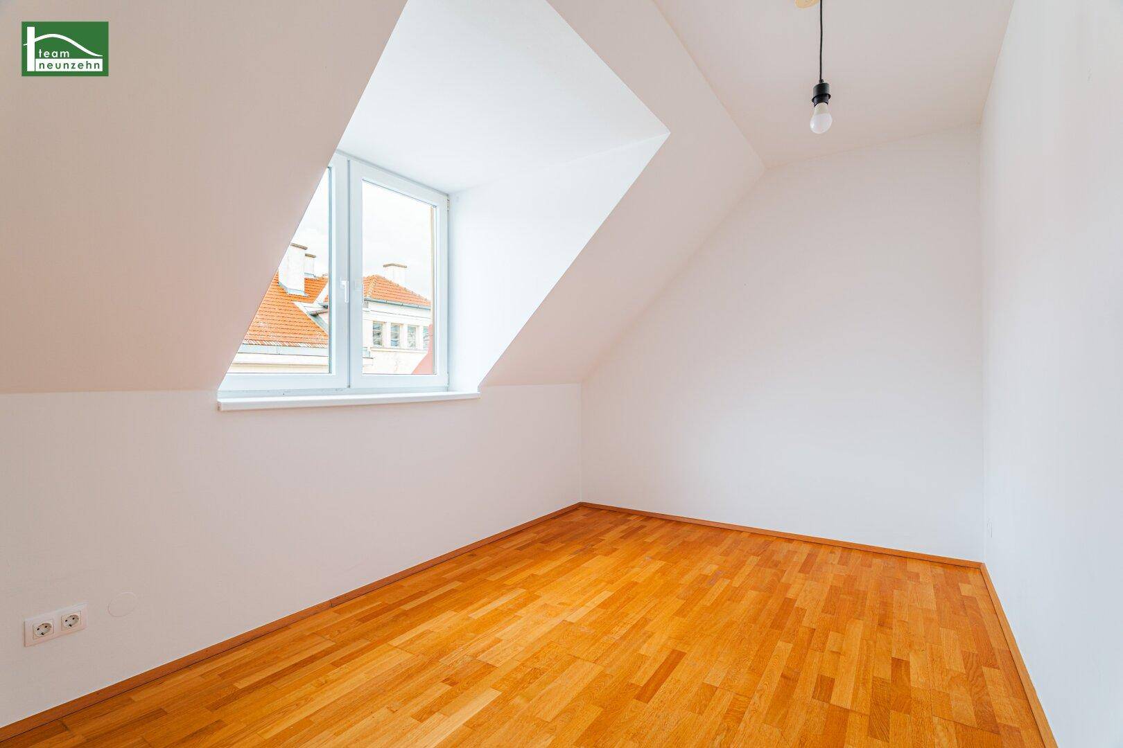 Dachzimmer mit Holzboden und schrägen Wänden, bietet eine ruhige Atmosphäre und Tageslicht.
