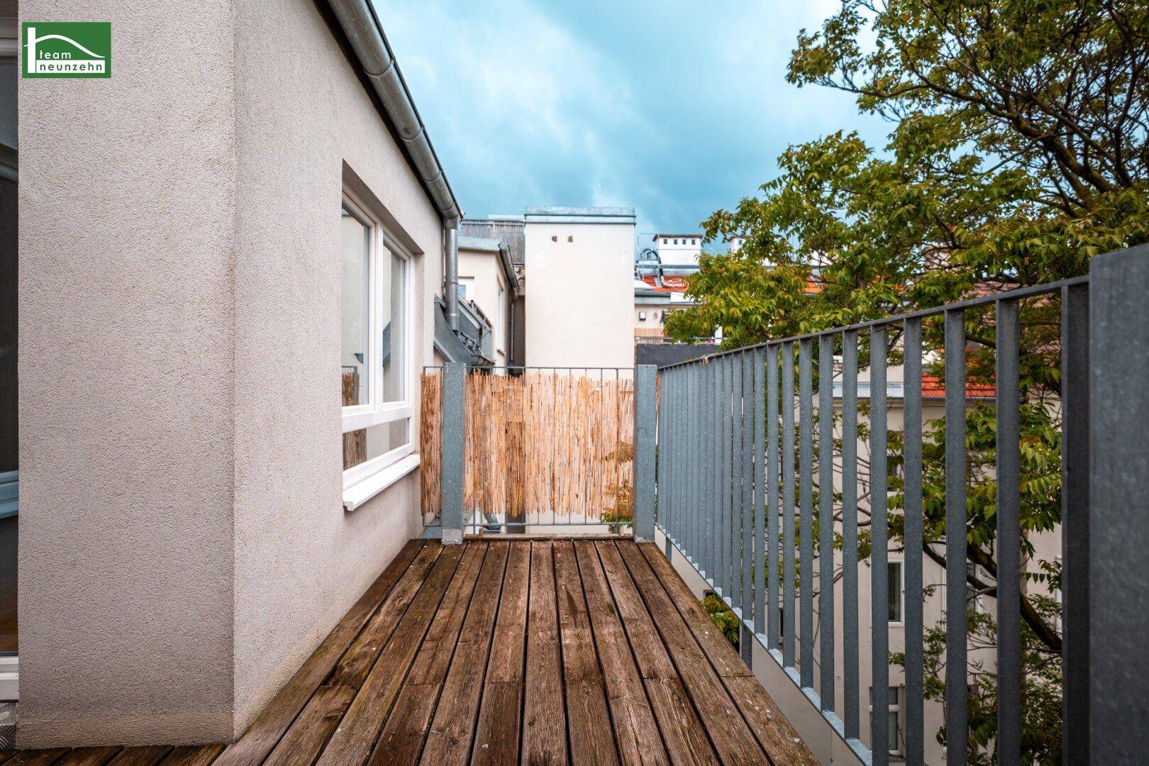 Langer Holzbalkon mit Metallgeländer und Blick auf die umliegende Bebauung und Bäume.