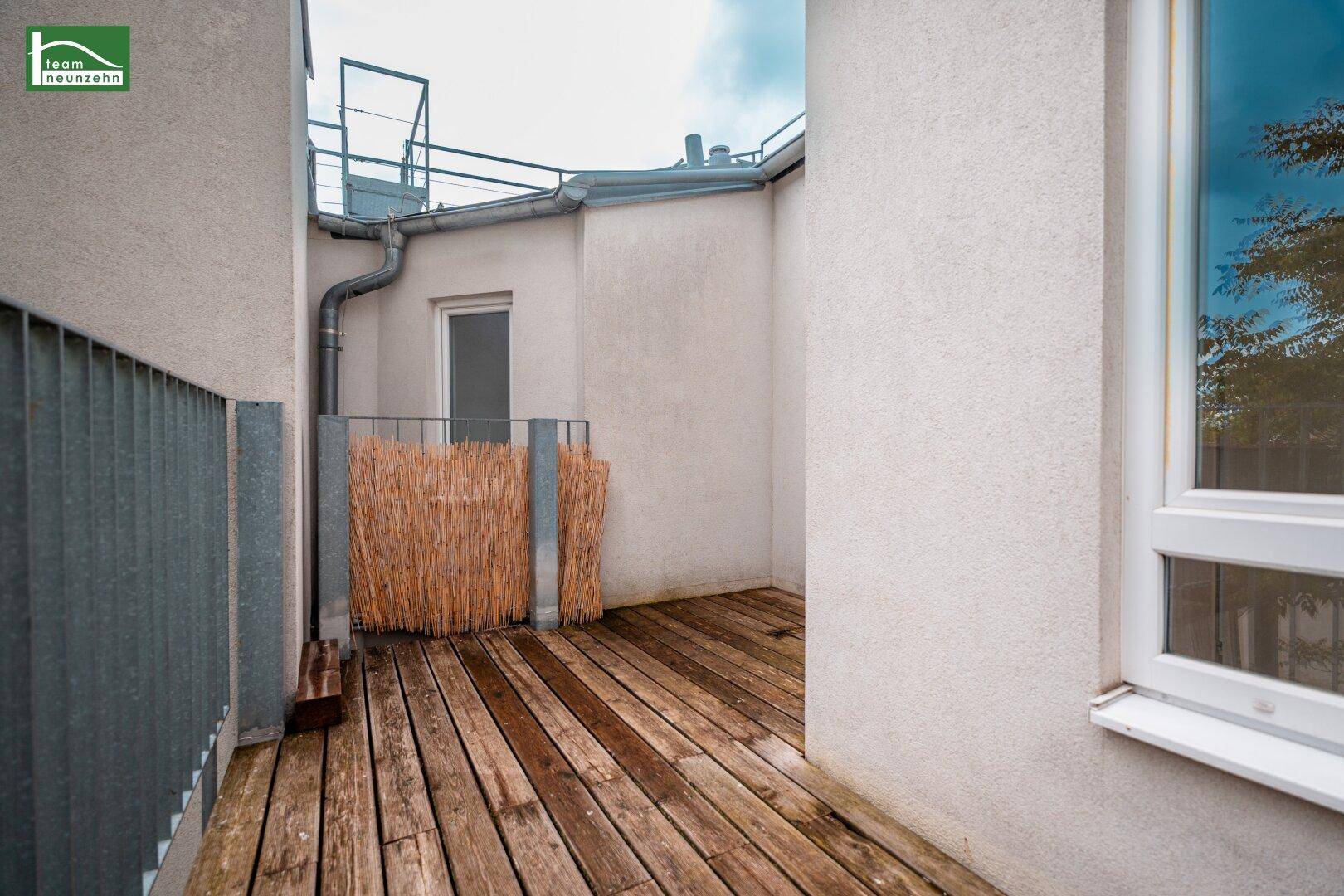Geräumiger Holzbalkon mit Sichtschutz und Blick auf die umliegenden Gebäude.