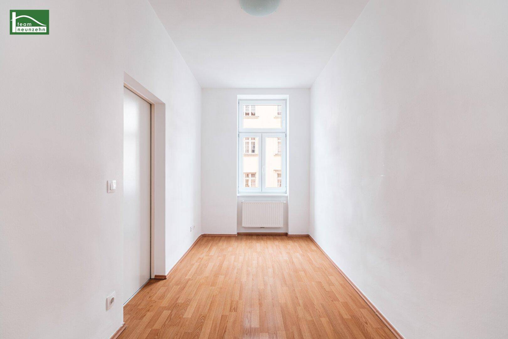 Helles, schmales Zimmer mit einem Fenster und Holzboden, ideal als Schlaf- oder Arbeitszimmer.