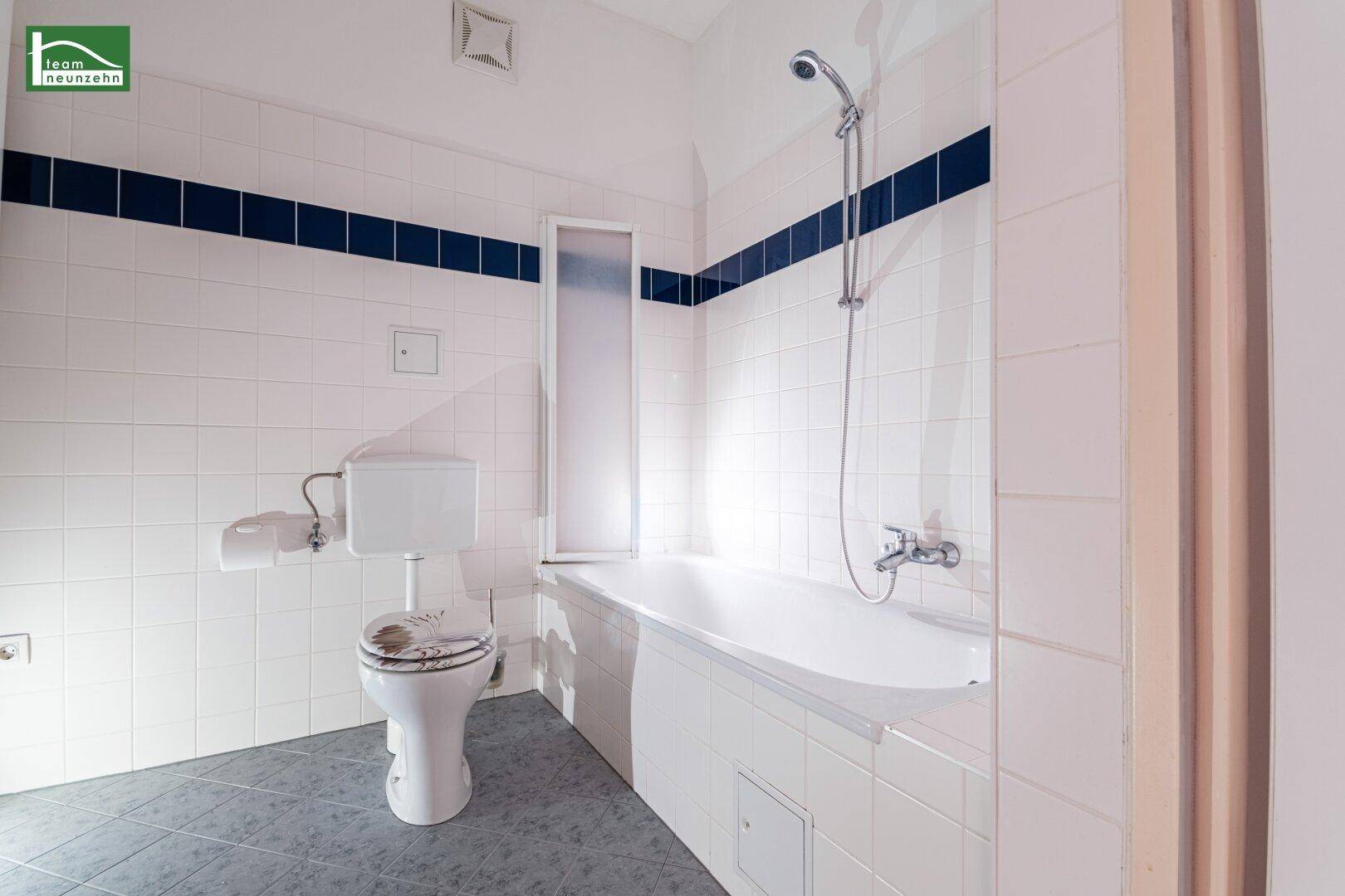 Badezimmer mit Badewanne, Dusche und WC, ausgestattet mit weißen Fliesen und blauen Akzenten.