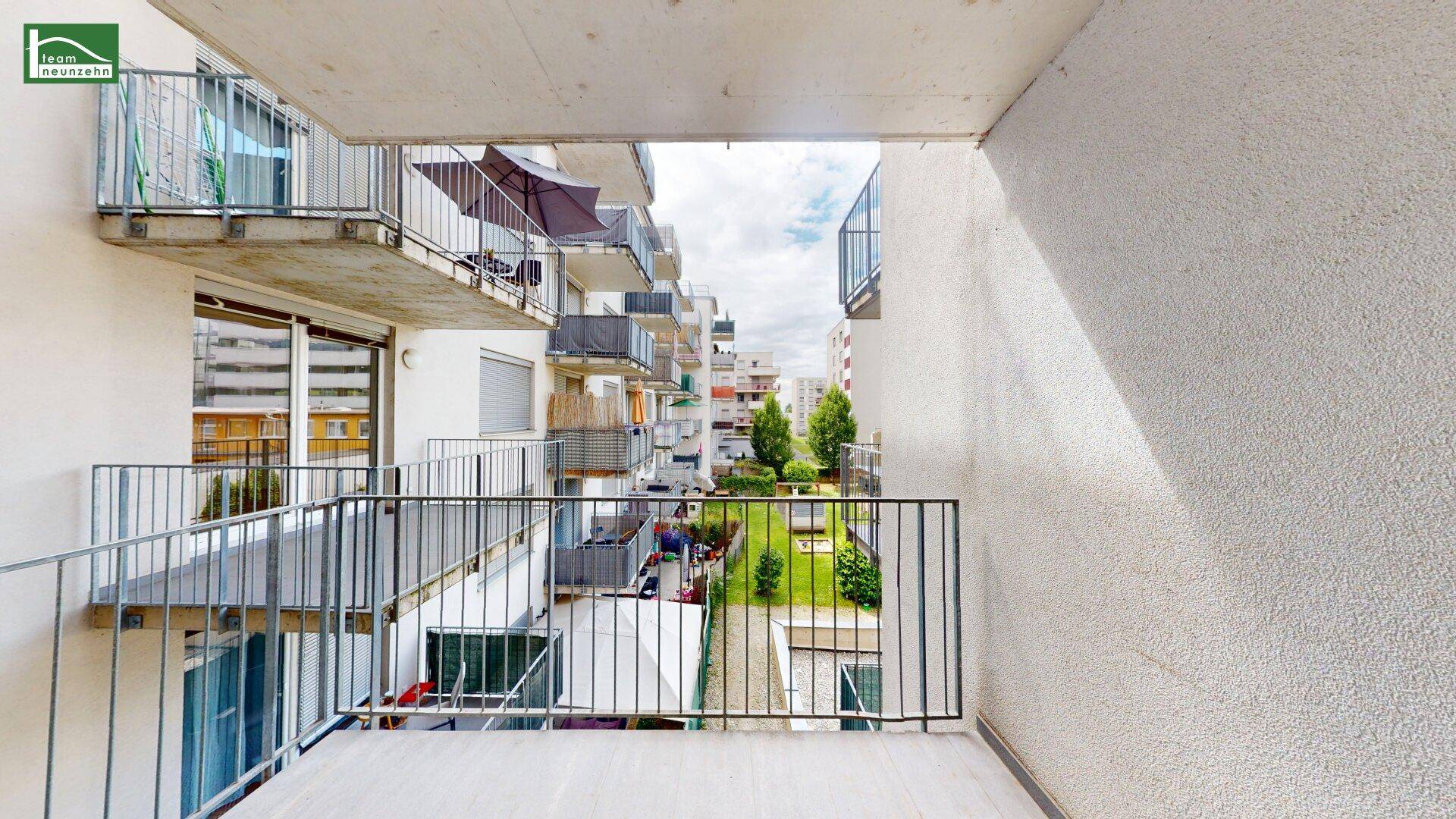 Balkon mit Metallgeländer und Blick auf den begrünten Innenhof der Wohnanlage.