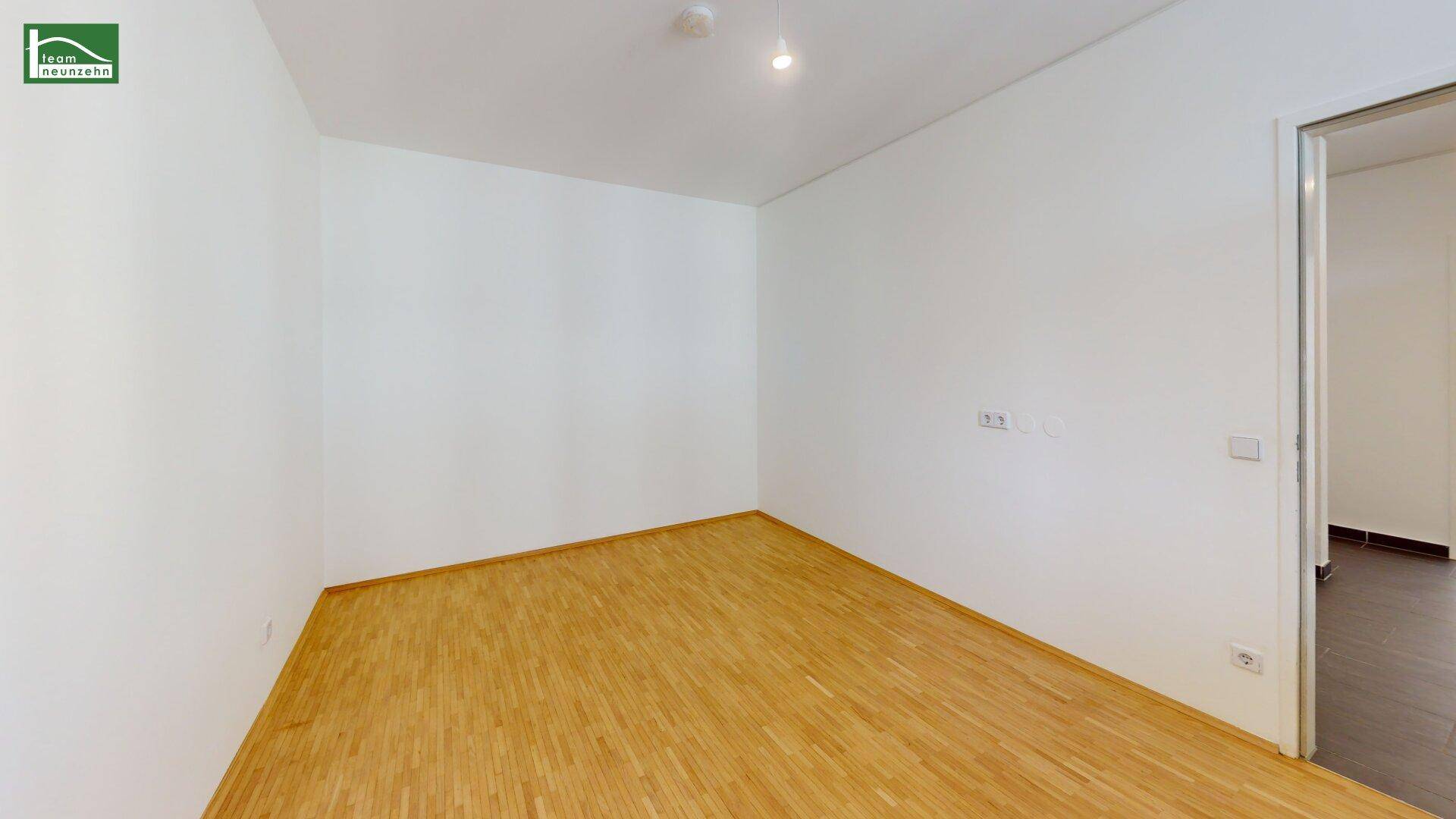 Leeres Schlafzimmer mit Parkettboden und Zugang zu einem weiteren Raum.