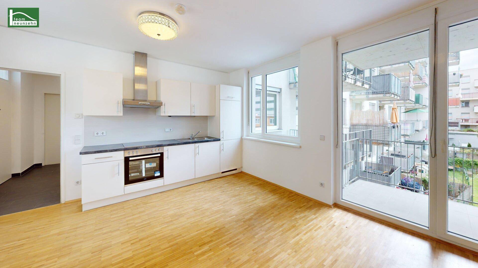 Helle Wohnküche mit modernen weißen Schränken, Holzboden und Zugang zum Balkon.