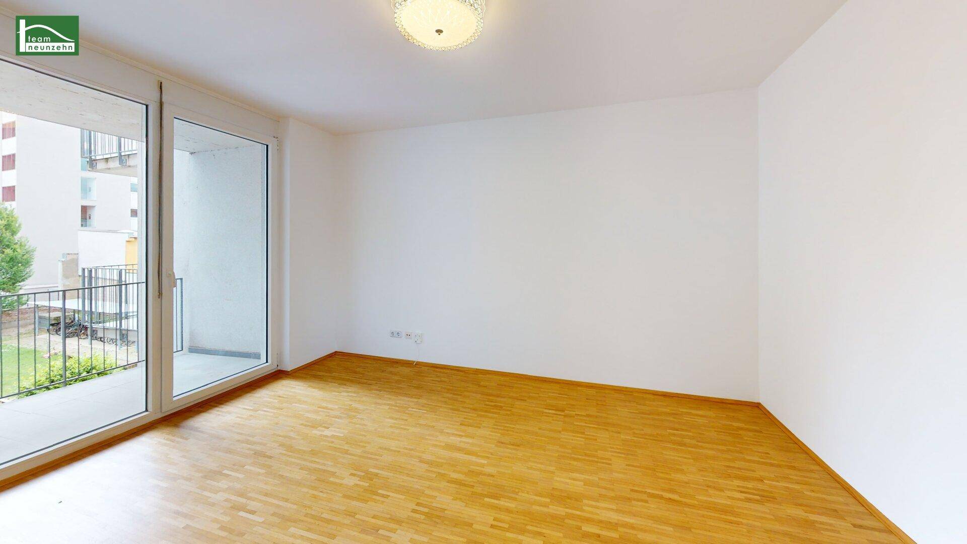 Leerer Wohnbereich mit Parkettboden und Zugang zu einem Balkon.