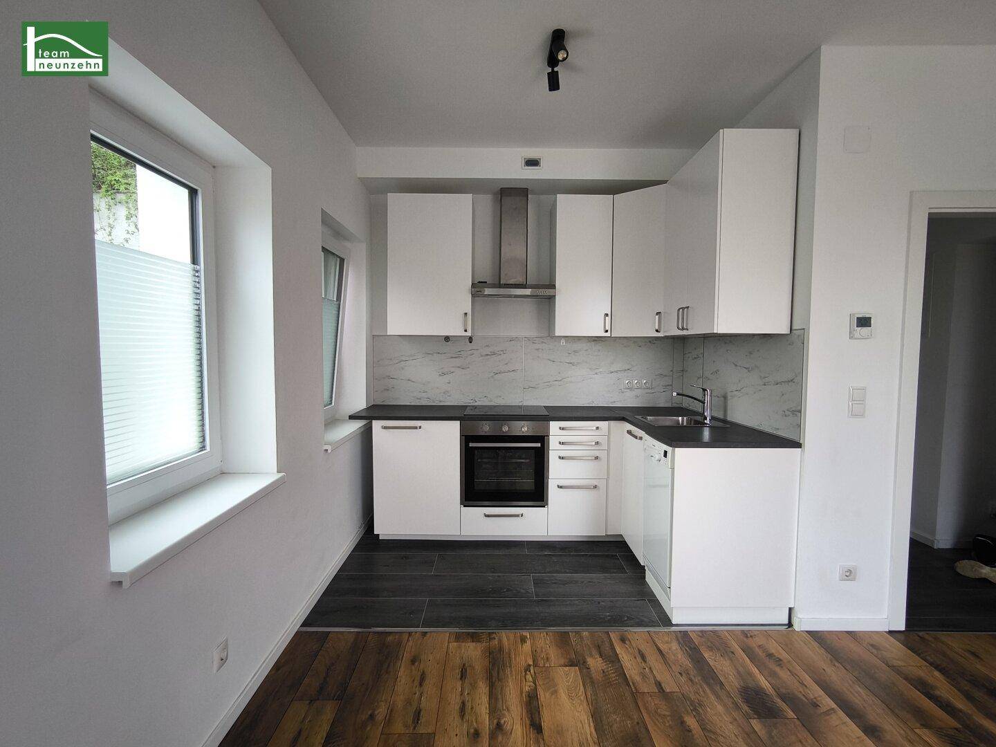 Moderne Einbauküche mit weißen Schränken, dunkler Arbeitsplatte und integriertem Backofen.