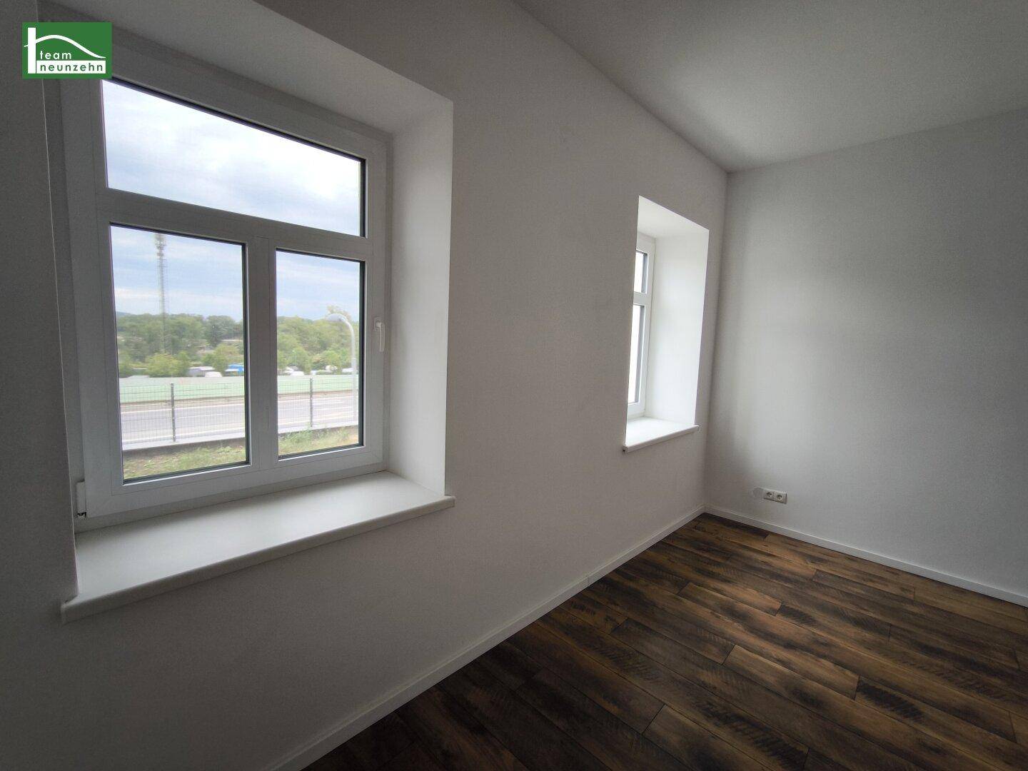 Heller Raum mit Laminatboden und Fenstern, die einen Blick auf die Umgebung bieten.