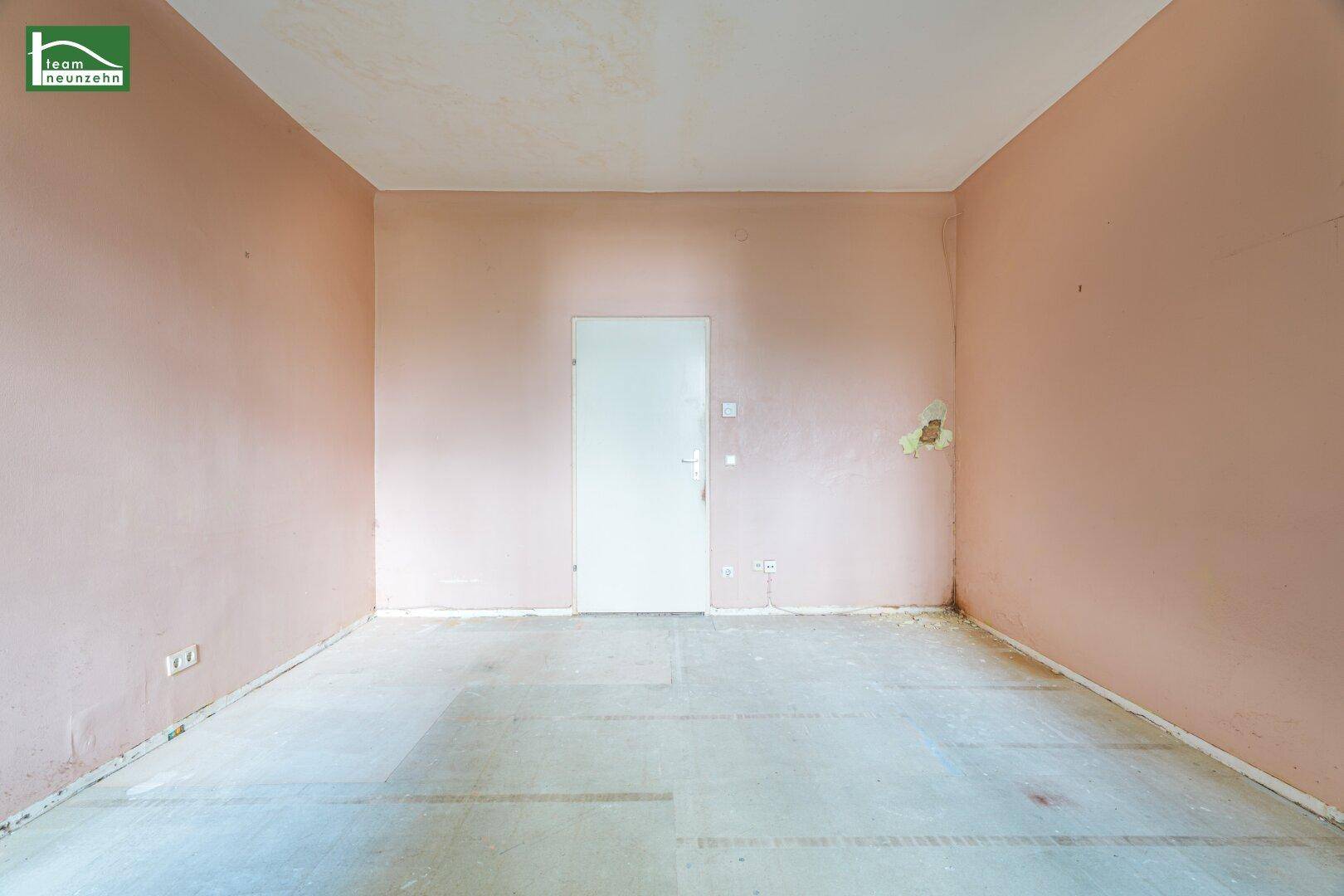 Leerer Raum mit rosa Wänden und einer weißen Tür, der auf eine Neugestaltung wartet.