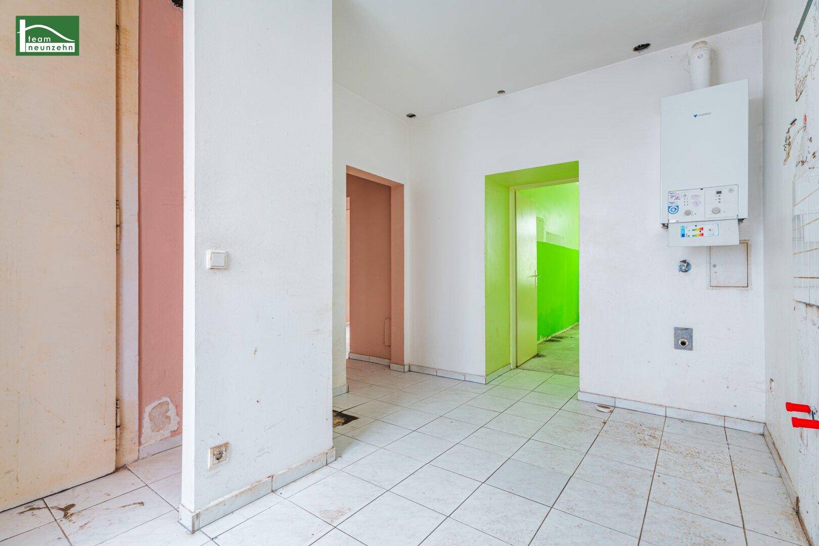 Flur mit weißen Fliesen, Gastherme an der Wand und Zugang zu verschiedenen Räumen.