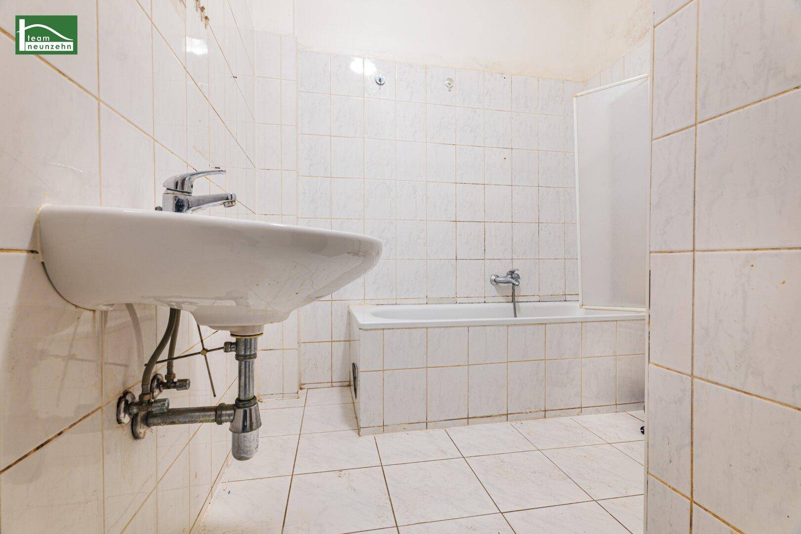Badezimmer mit weiß gefliesten Wänden, Waschbecken und einer Badewanne mit Duschabtrennung.