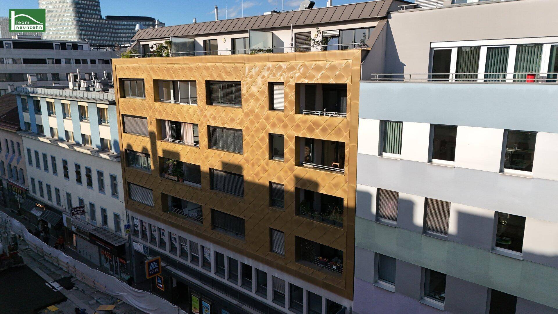 Ansicht einer modernen Gebäudefassade mit goldfarbenen Paneelen und zahlreichen Fenstern.