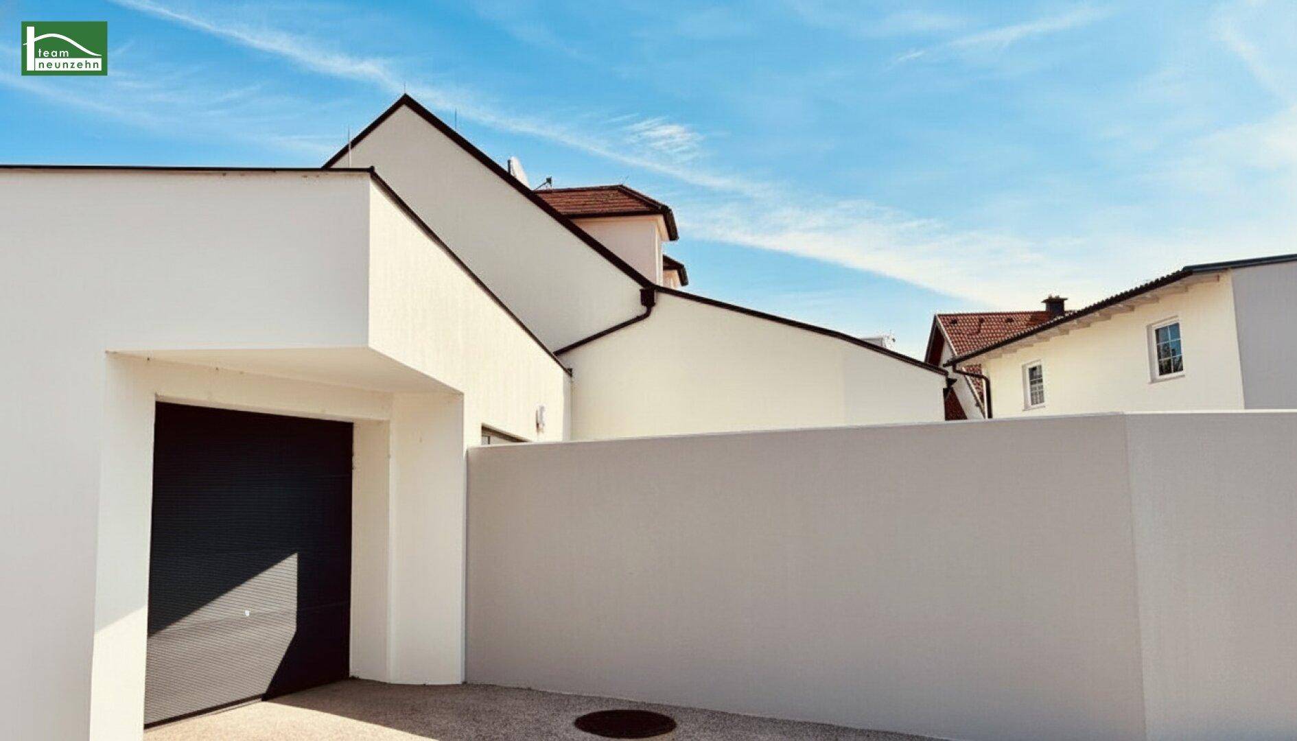Garagenzufahrt mit modernem Tor und weißer Mauer, die das Grundstück begrenzt.