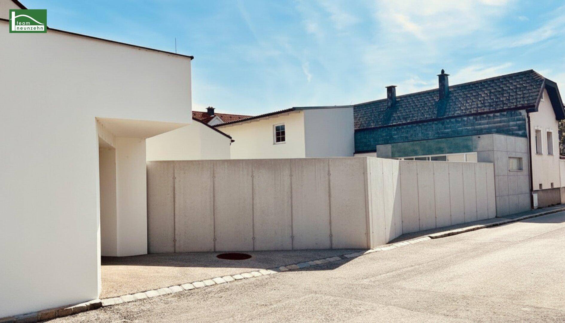 Seitenansicht des Anwesens mit einer modernen Betonmauer und Garagenzufahrt.