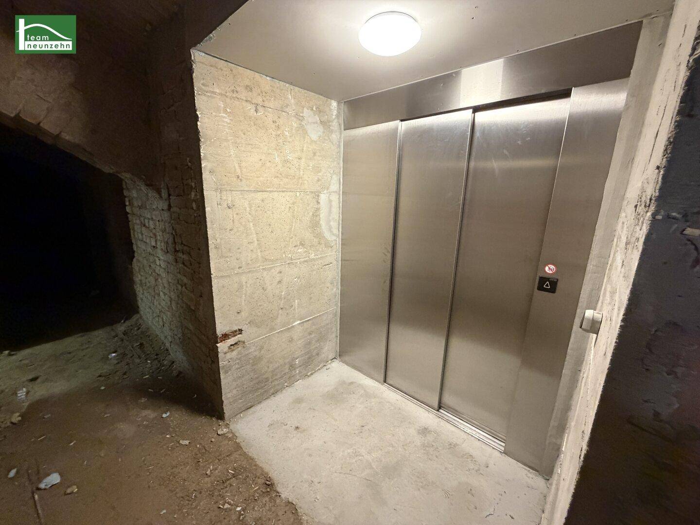 Moderner Aufzug in einem Rohbau-Kellerbereich mit Betonwänden.