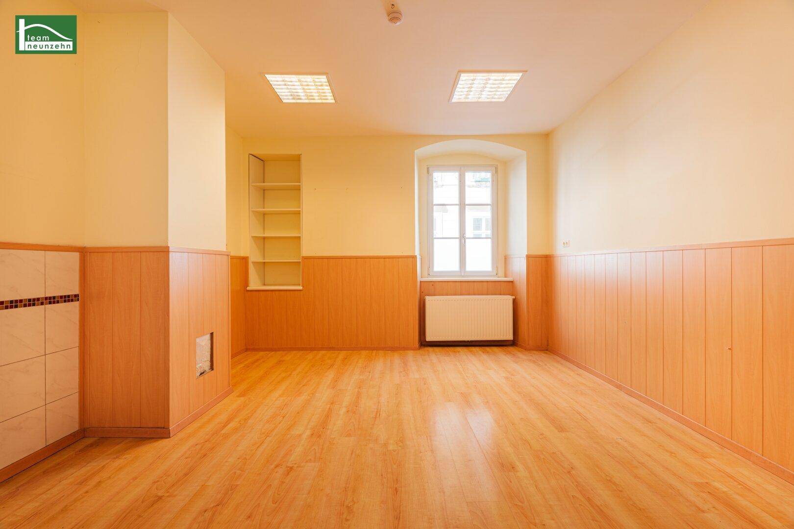 Heller Raum mit Laminatboden, Holzpaneelen und einem Fenster, inklusive Wandregal.