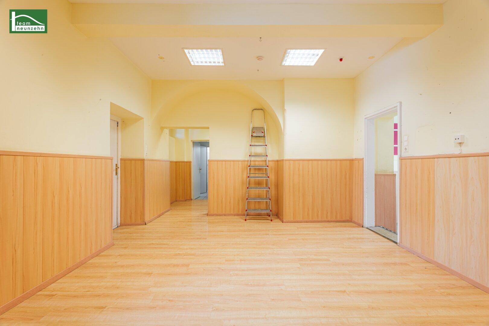 Heller, offener Raum mit Laminatboden und Holzpaneelen, mit einer Leiter im Hintergrund.
