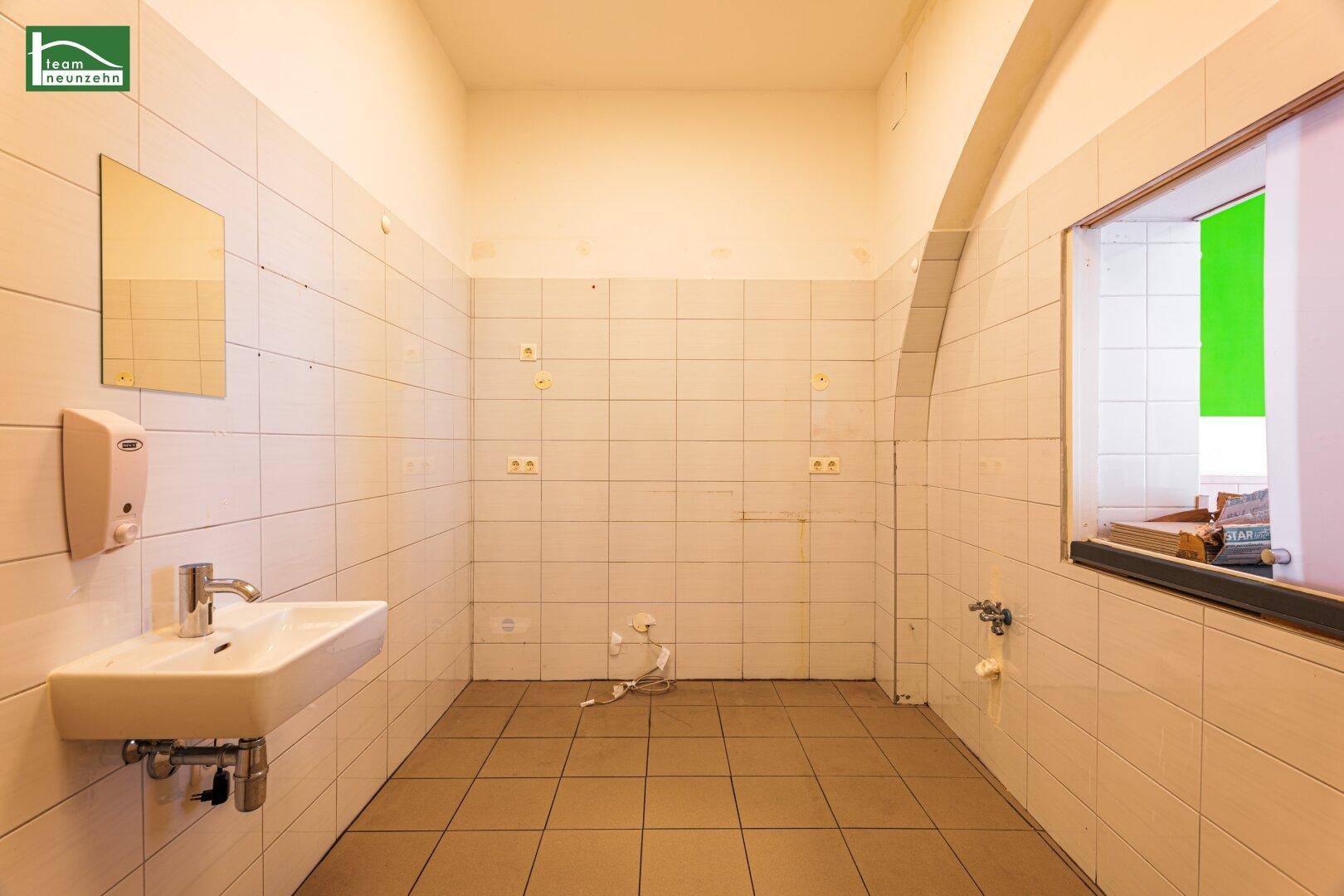 Gefliester Waschraum mit Waschbecken und Spiegel, bereit für die Installation weiterer Sanitäranlagen.