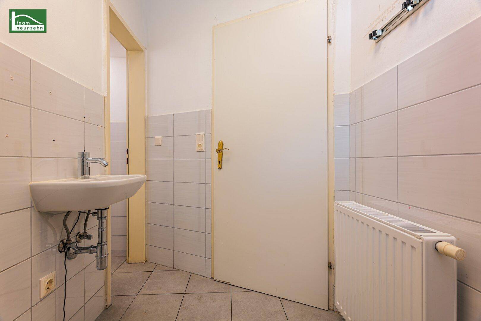 Gefliester Waschraum mit Waschbecken und Heizkörper, mit Zugang zu einer Toilette.