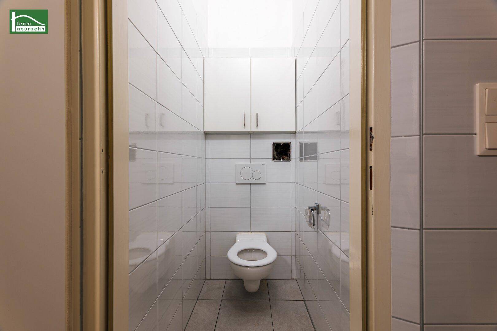 Separate Toilette mit Wand-WC und Spülkasten, in einem gefliesten Raum.