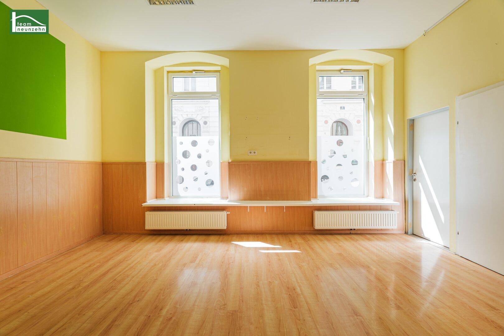 Heller, geräumiger Raum mit Laminatboden und zwei großen Fenstern zur Straße.